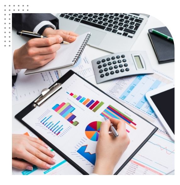 Two hands analyze colorful charts on a clipboard, surrounded by notebooks, a calculator, and a laptop in a business setting.